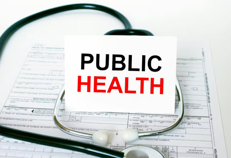 Stock image of a stethoscope on top of a page of gridded paper. The stethoscope is proping up a white card that reads "Public Health" in black and red letters
